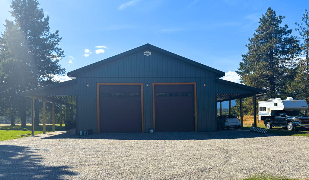 A dark sage post-frame shop with open lean-tos, soffits, and wooden trims