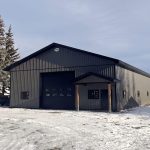 A charcoal post-frame lifestyle and agricultural shop with open lean-to porch, and an overhead door