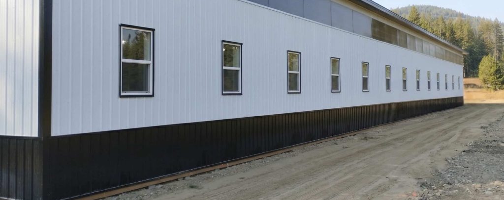 A bright white post-frame equestrian riding arena with black wainscoting
