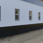 A bright white post-frame equestrian riding arena with black wainscoting