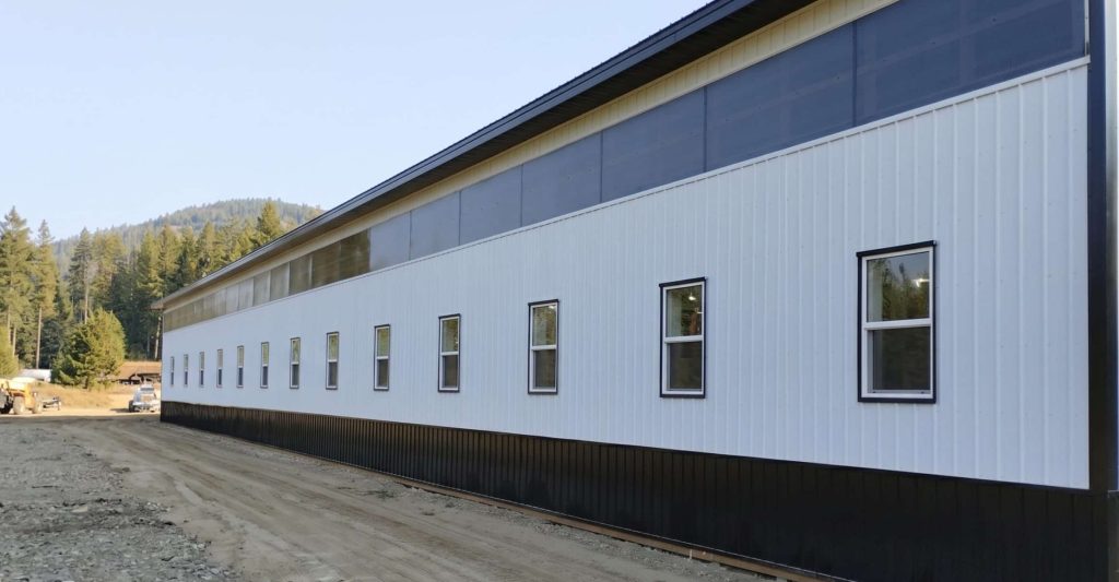 A bright white post-frame equestrian riding arena with black wainscoting