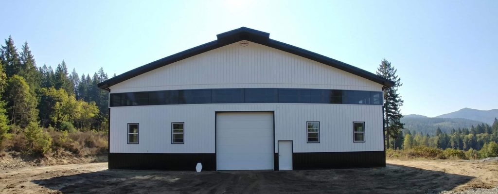 A bright white post-frame equestrian riding arena with black wainscoting