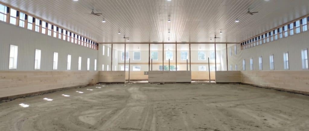A bright white post-frame equestrian riding arena with black wainscoting