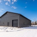 A charcoal post-frame lifestyle and agricultural shop with open lean-to porch, and an overhead door
