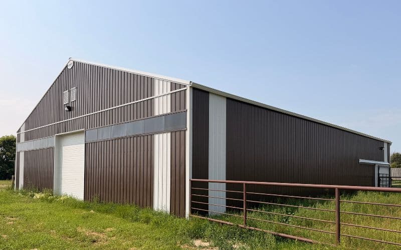 A coffee brown post-frame livestock shelter with overhead and sliding doors