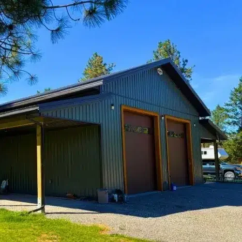 A dark sage post-frame shop with open lean-tos, soffits, and wooden trims