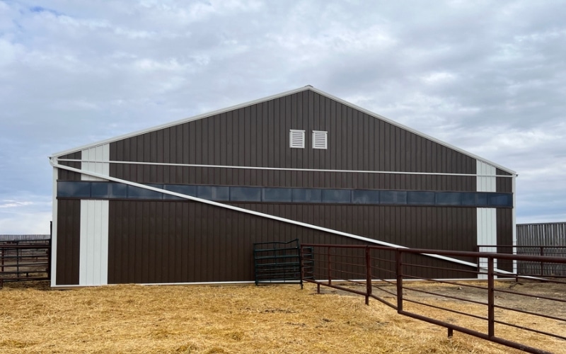 A coffee brown post-frame livestock shelter with wall lights and a sliding door