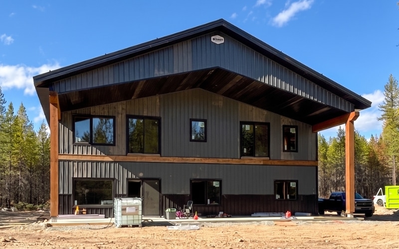 A gunmetal post-frame residential shouse with a front porch, soffits, and black wainscoting