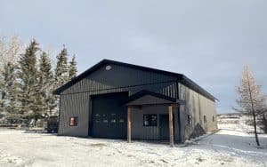 A charcoal post-frame lifestyle and agricultural shop with open lean-to porch, and an overhead door