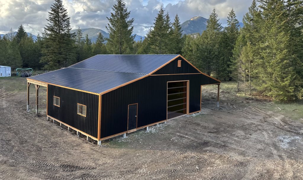 A black post-frame shop with copper penny trims and an overhead door