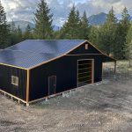 A black post-frame shop with copper penny trims and an overhead door