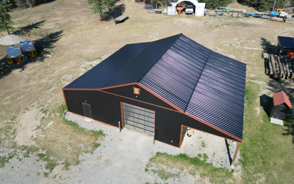 A black post-frame shop with copper penny trims and an overhead door