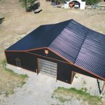 A black post-frame shop with copper penny trims and an overhead door