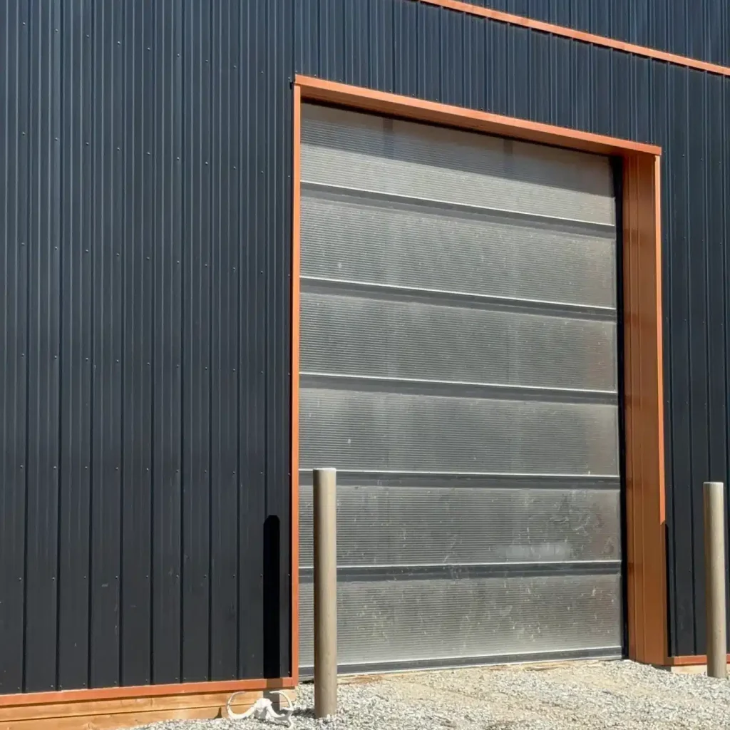 A black post-frame shop with copper penny trims and an overhead door