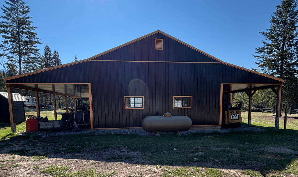 A black post-frame shop with copper penny trims and an overhead door