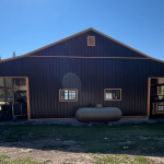 A black post-frame shop with copper penny trims and an overhead door