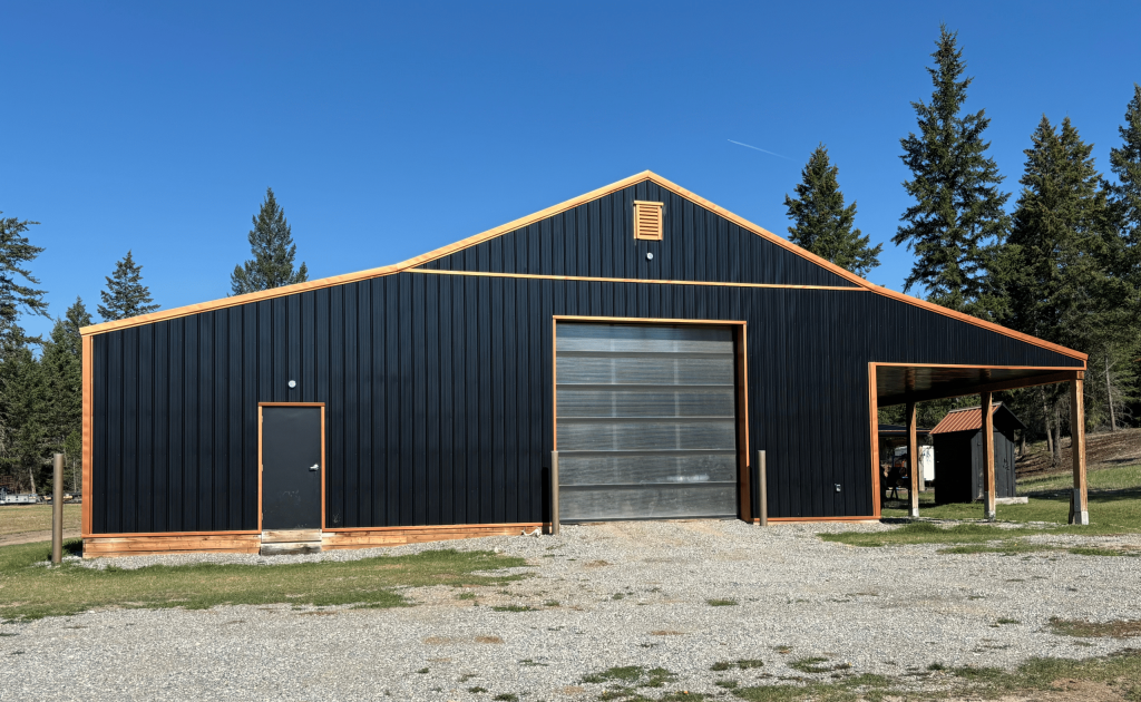 A black post-frame shop with copper penny trims and an overhead door
