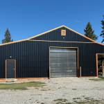 A black post-frame shop with copper penny trims and an overhead door