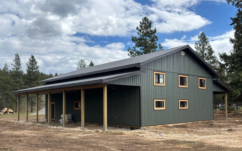 A dark sage post-frame shop with open lean-tos, soffits, and wooden trims