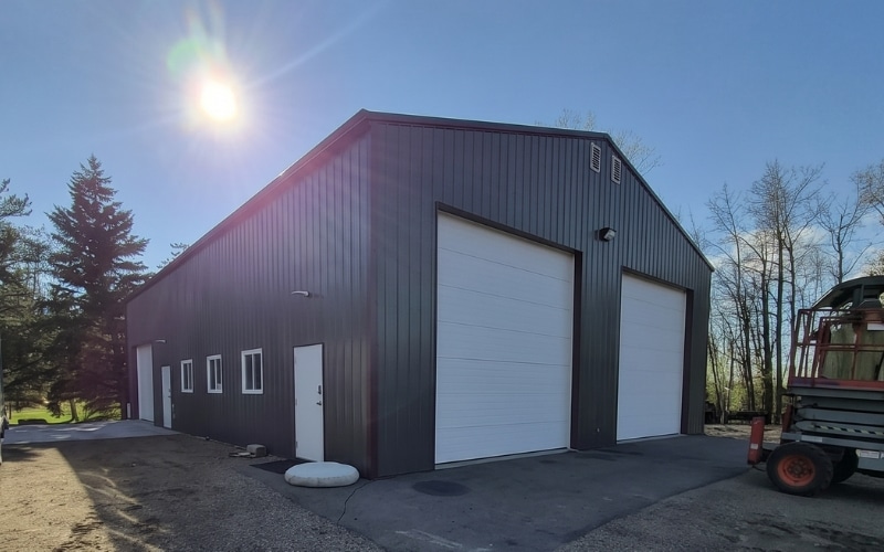 A dark sage post-frame agriculture storage shop with overhead doors and soffits