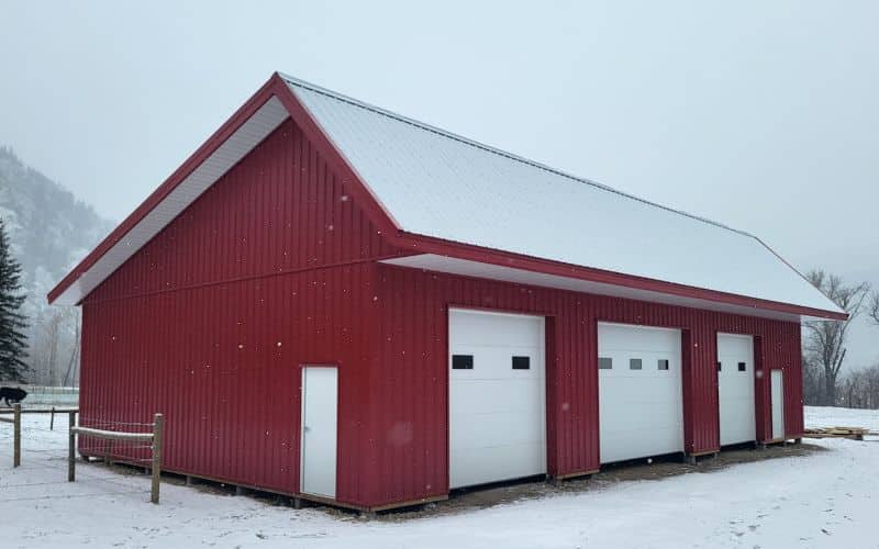 A dark red post-frame lifestyle shop with soffits and overhead doors