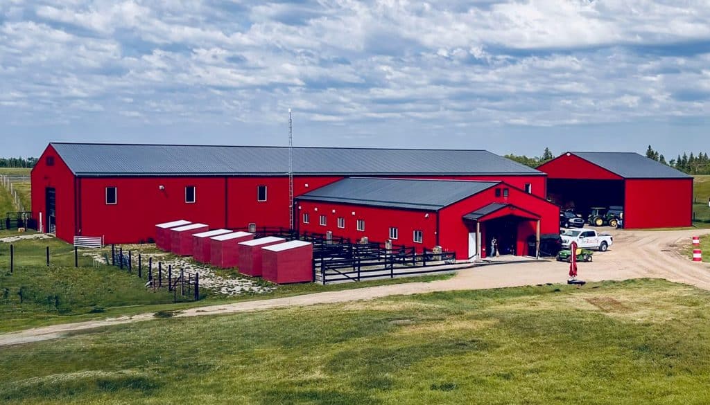 Post-frame riding arena in bright red cladding with an attached barn