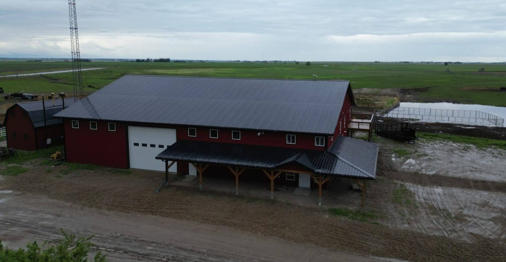 A dark red post-frame equestrian barn and office with open lean-to and deck