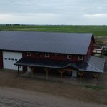 A dark red post-frame equestrian barn and office with open lean-to and deck