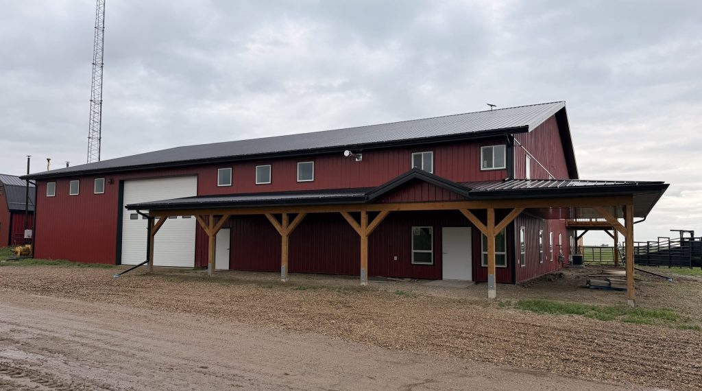 A dark red post-frame equestrian barn and office with open lean-to and deck