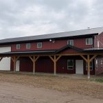 A dark red post-frame equestrian barn and office with open lean-to and deck