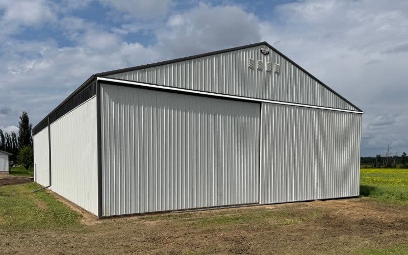 A white white post-frame agriculture storage with a sliding door and wall lights