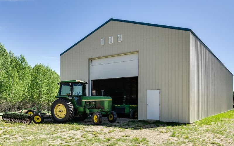 A wicker post-frame hay shed storage building with a slate blue roof