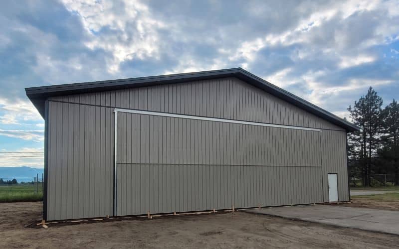 A stone grey post-frame agricultural airplane hangar