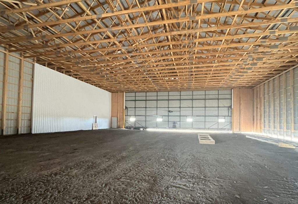 A bone white post-frame agricultural storage building with bi-fold door