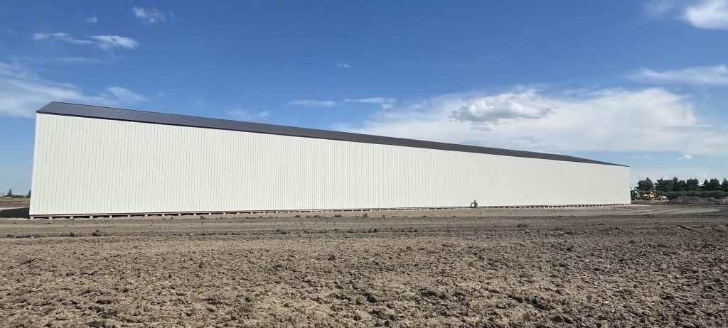 A bone white post-frame agricultural storage building with bi-fold door