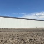 A bone white post-frame agricultural storage building with bi-fold door
