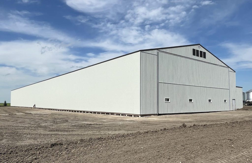 A bone white post-frame agricultural storage building with bi-fold door