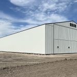 A bone white post-frame agricultural storage building with bi-fold door
