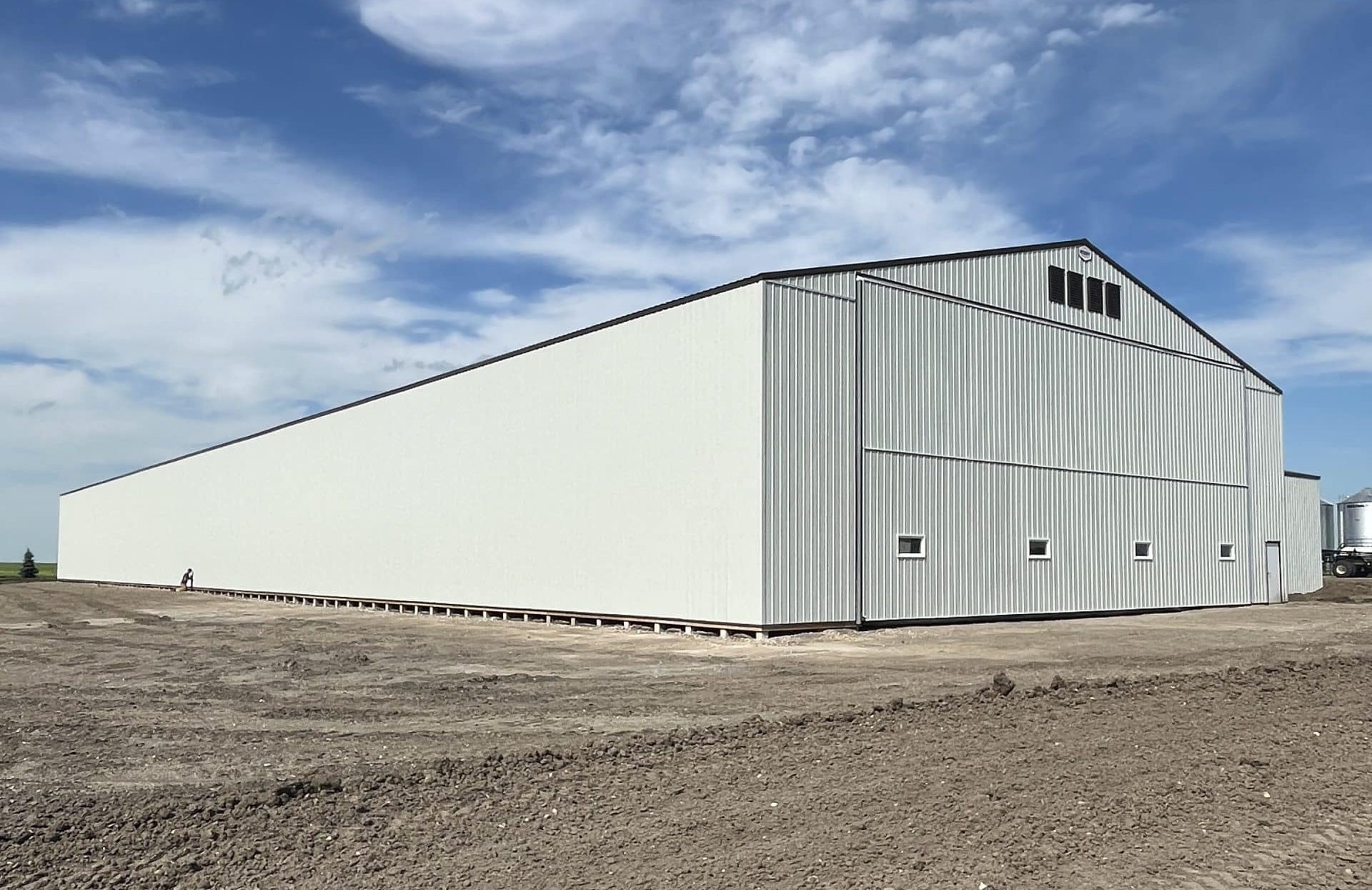 A bone white post-frame agricultural storage building with bi-fold door