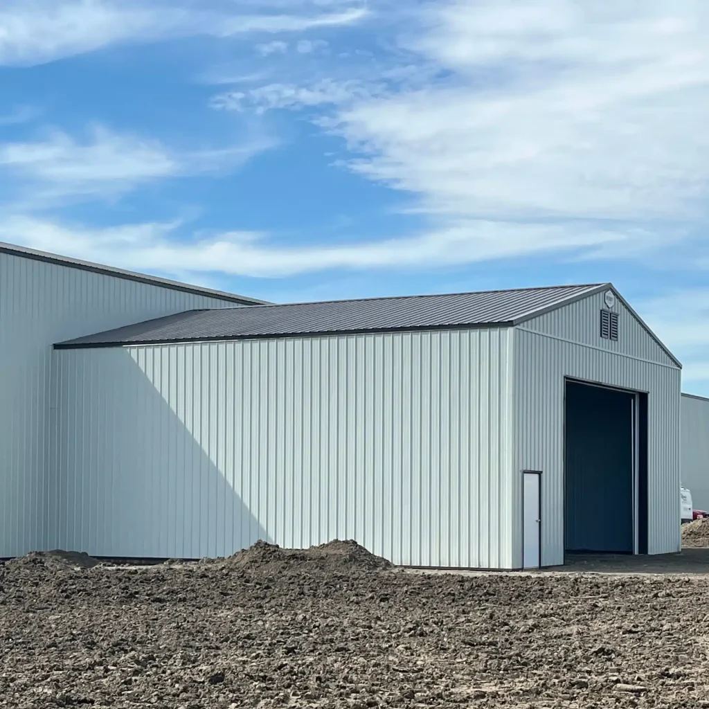 A bone white post-frame agricultural storage building with bi-fold door