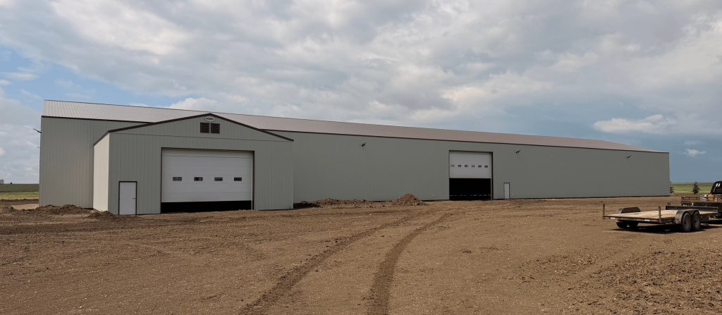 A bone white post-frame agricultural storage building with bi-fold door