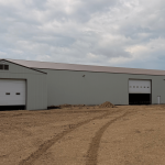 A bone white post-frame agricultural storage building with bi-fold door