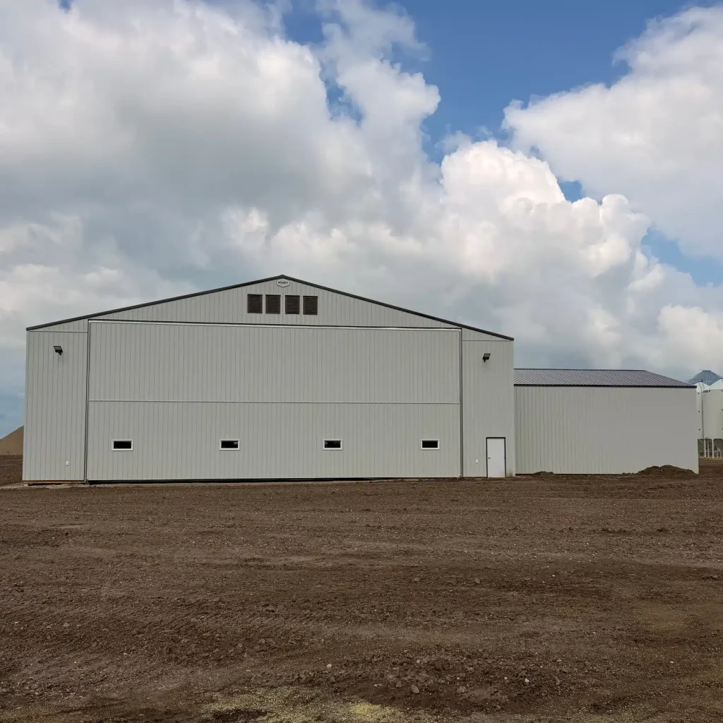 A bone white post-frame agricultural storage building with bi-fold door
