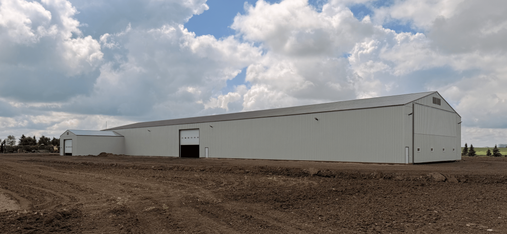 A bone white post-frame agricultural storage building with bi-fold door