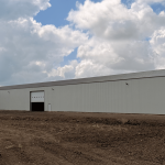 A bone white post-frame agricultural storage building with bi-fold door
