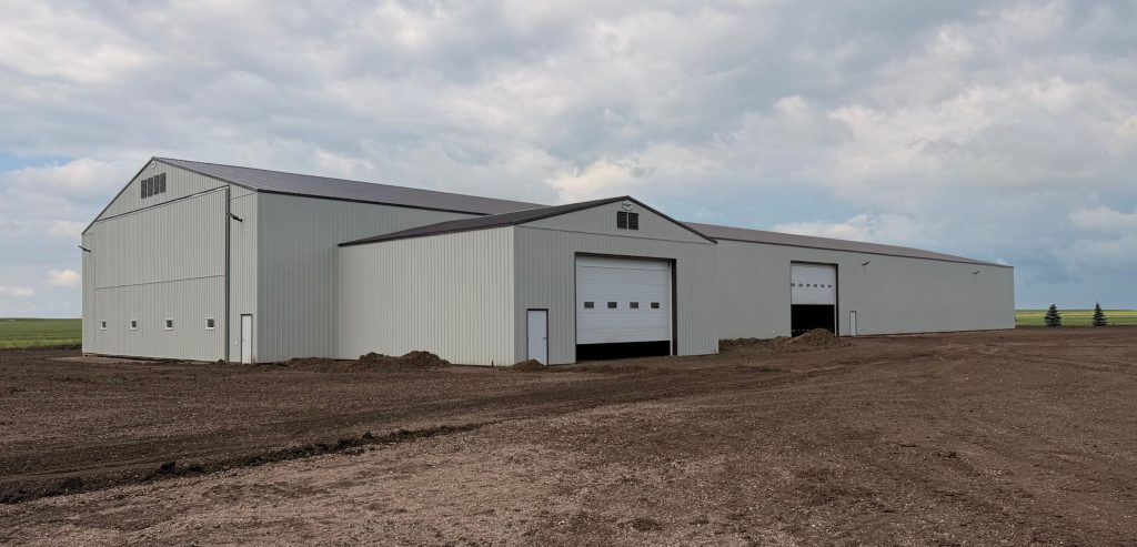 A bone white post-frame agricultural storage building with bi-fold door