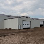 A bone white post-frame agricultural storage building with bi-fold door