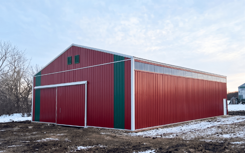 A dark red post-frame livestock shelter with sliding doors