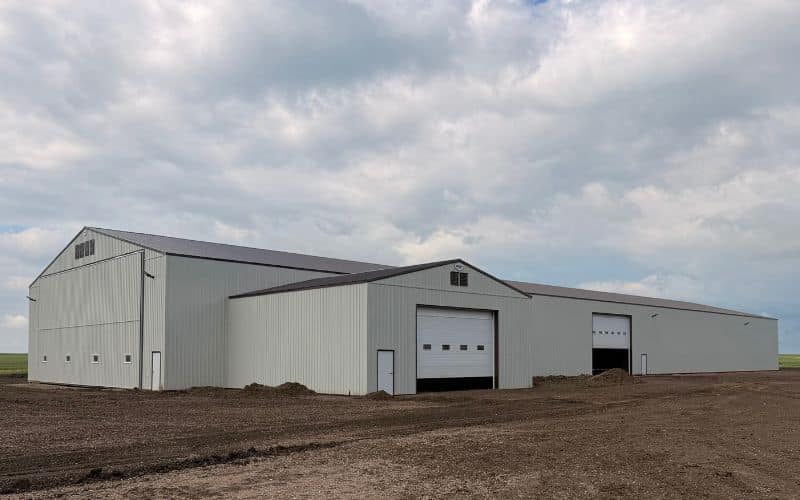 A bone white post-frame agricultural storage building with bi-fold door