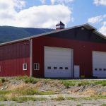 A dark red post-frame agriculture storage building with cupolas